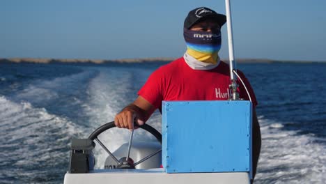Mittlere-Aufnahme,-Mann-Mit-Rotem-Hemd-Fährt-Das-Boot-Im-Fluss-Von-Adolfo-Lopez-Mateos-Baja-California-Sur,-Mexiko,-Malerische-Aussicht-Auf-Blauen-Himmel-Und-Strahlend-Sonnigen-Tag-Im-Hintergrund