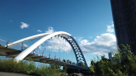 Wide-low-angle-time-lapse-of-people-traffic-on-the-majestic-Humber-Bay-Arch-Bridge,-set-against-the-moving-sky