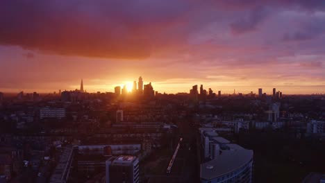 Un-Dron-Aéreo-Disparó-Hacia-Los-Rascacielos-De-La-Ciudad-De-Londres-Mientras-El-Tren-Pasa-Debajo-Del-Atardecer.