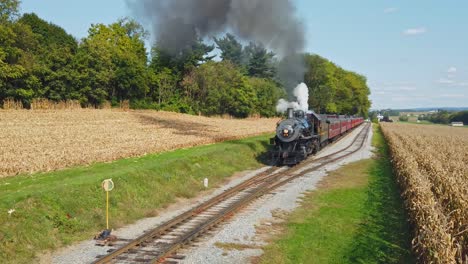 Una-Antigua-Locomotora-Restaurada-Y-Vagones-De-Pasajeros-Que-Se-Acercan-En-Un-Día-Soleado-Viajando-Por-El-Campo-Visto-Desde-Una-Altura-Elevada