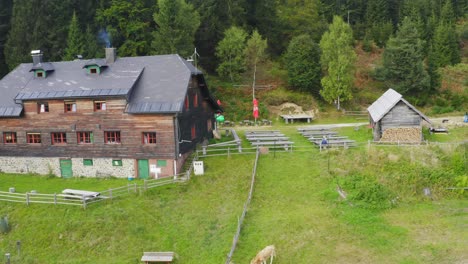 Toma-Aérea-De-Una-Gran-Casa-De-Madera-Con-Una-Granja-Cerca-Del-Bosque-En-Sostanj