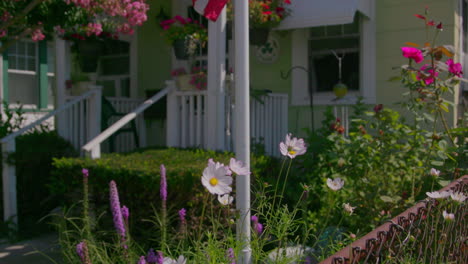 Tilt-up-on-a-flag-pole-with-an-American-flag,-with-flowers-in-the-garden-on-a-sunny-day
