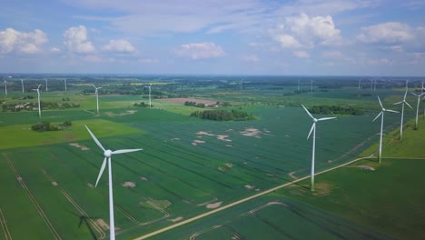 Aerial-view-of-wind-turbines-generating-renewable-energy-in-the-wind-farm,-sunny-summer-day,-lush-green-agricultural-cereal-fields,-countryside-roads,-wide-angle-drone-shot-moving-forward