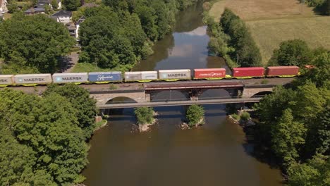 Langer-Bunter-Güterzug,-Der-An-Einem-Sonnigen-Tag-In-Deutschland-Eine-Flussbrücke-überquert