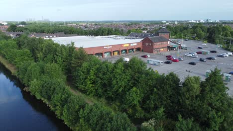 Aerial-view-flying-above-canal-reveal-Morrisons-supermarket-car-park-in-rural-Warrington-countryside-village