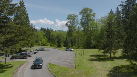 Car-drives-out-of-rest-stop-parking-lot-and-towards-camera-with-boom-up-to-reveal-Bellingham,-Washington-landscape-and-horizon-on-a-gorgeous-day