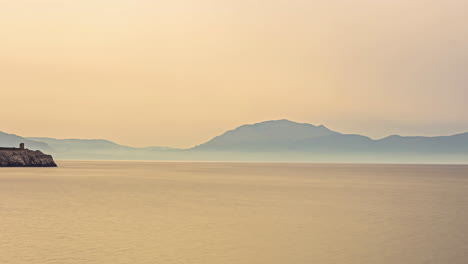 Ruhiger,-Pastellorangefarbener-Sonnenuntergangshimmel-über-Dem-Friedlichen-Meer-Mit-Bergen