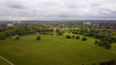 Volando-Sobre-Un-Terreno-Común-De-Londres-Hacia-Un-Estanque-De-Patos-Y-Casas-Al-Fondo