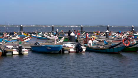 People-walking,-fishing-boats-moored-at-pier,-Ria-de-Aveiro,Torreira
