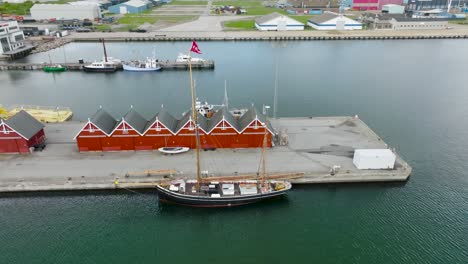 Aerial-view,-old-wooden-sailboat-moored-at-the-quays-in-the-port,-wooden-fishermans-warehouses-stand-on-the-quays