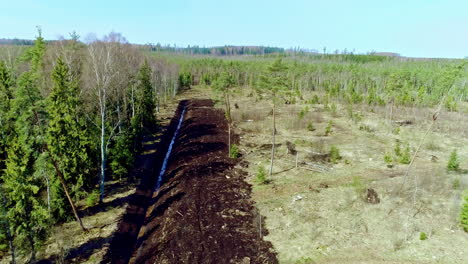 Toma-Aérea-En-Movimiento-De-Un-Estrecho-Canal-De-Agua-A-Través-De-Un-Bosque-Verde-A-Lo-Largo-Del-Campo-Rural-Durante-El-Día