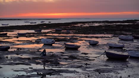 Wunderschöne-Sonnenuntergangslandschaft-Bei-Ebbe-Mit-Fischerbooten-Und-Weiblicher-Silhouette