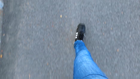 Vista-De-Arriba-Hacia-Abajo-De-La-Persona-Que-Camina,-Movimiento-Bípedo-De-Marcha-De-Piernas-Y-Pies,-Caminata-Peatonal-En-La-Acera,-Jeans-Azules-Y-Zapatos-Adidas-Negros