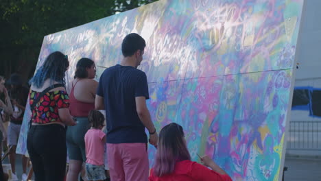 Plano-Medio-De-Un-Grupo-Multicultural-De-Personas-Pintando-Un-Gran-Lienzo-En-Un-Parque-Público.