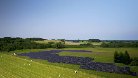 Aufsteigende-Luftaufnahme-Umweltfreundlicher-Sonnenkollektoren-Auf-Der-Grünen-Wiese-In-Polen-An-Einem-Schönen-Sonnigen-Tag-Und-Blauem-Himmel