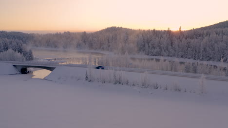 Aerial-view-vehicle-crossing-quiet-snowy-Sweden-mountain-landscape-at-sunrise-through-frosty-wilderness