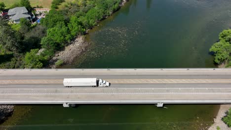 Toma-Aérea-De-Un-Semi-Camión-Cruzando-Un-Puente-Que-Pasa-Sobre-Un-Río-En-El-Estado-De-Washington