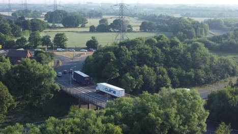 Vista-Aérea-De-La-Plataforma-Rodante-A-La-Derecha-Exuberante-Paisaje-Tierras-De-Cultivo-Bosques-Rurales-Autopista-M62,-Rainhill,-Inglaterra