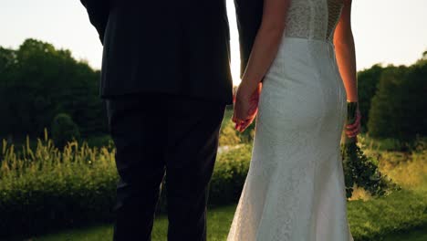 Close-up-of-wedding-couple-holding-hands-standing-still-as-the-sun-sets-over-scenic-landscape