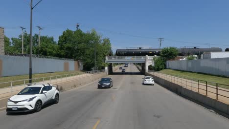 Traveling-in-the-Illinois-Chicago-land-area,-suburbs,-streets,-and-highways-in-POV-mode-under-bridge-and-train