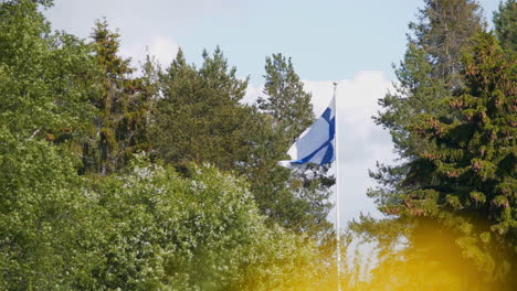 Slomo-of-flag-of-Finland-flying-in-typical-Finnish-nature-among-pine-trees