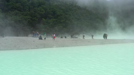 Gente-En-Una-Playa-En-Un-Cráter-De-Volcán-Rodeado-Por-Un-Lago-De-Azufre-En-Kawah-Putih,-Antena