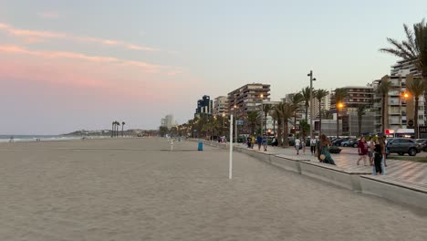 People-strolling-along-the-promenade-of-San-Juan-de-Alicante-next-to-the-beach-in-a-beautiful-sunset