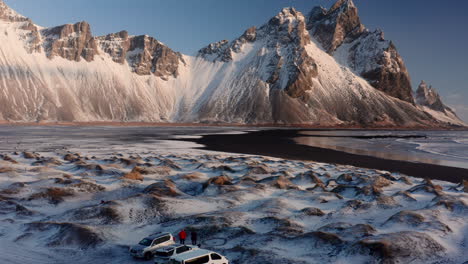 Backwards-shot-of-snowy-dunes,-black-beach-and-snowy-golden-Vestrahorn-Mountains-on-Iceland