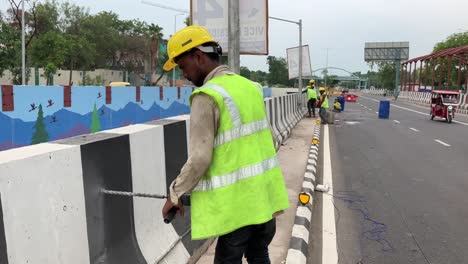 Un-Trabajador-De-La-Construcción-Perfora-Un-Agujero-En-Un-Divisor-De-Carreteras-En-Una-Carretera-Muy-Transitada