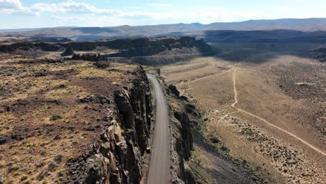 Toma-Aérea-Siguiendo-Una-Carretera-Excavada-En-La-Ladera-De-Una-Montaña-En-El-Desierto