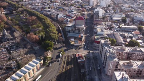 Nach-Unten-Geneigte-Luftaufnahme-Des-Verkehrs-Auf-Der-Straße-Und-Des-Zuges-Auf-Der-Schiene-In-Der-Nähe-Des-Bahnhofs-Chacarita-Und-Des-Friedhofs-In-Buenos-Aires