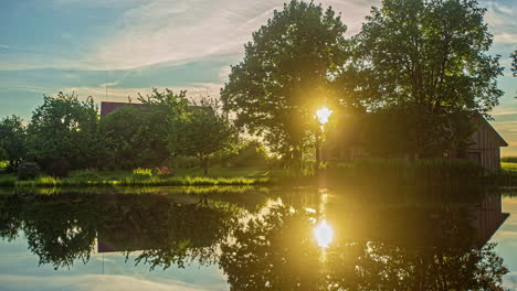 Timelapse-shot-of-sunset-over-river-water-passing-beside-a-wooden-cottages-in-background