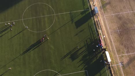 Vista-Aérea-De-Arriba-Hacia-Abajo-Del-Campo-De-Fútbol-Con-Jugadores-Al-Atardecer