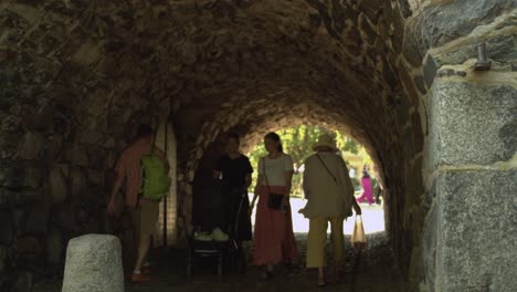 People-walk-through-long-medieval-stone-arch-tunnel-on-sunny-day