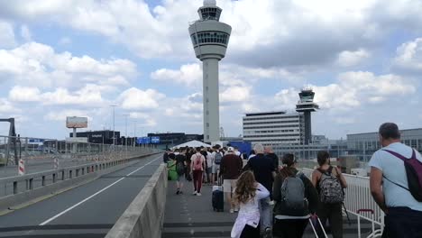 Cola-De-Personas-Caminando-Para-Abordar-Cerca-De-Las-Torres-De-Control-En-La-Pista-Del-Aeropuerto-Schiphol-De-Amsterdam