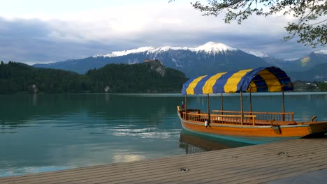 Toma-Panorámica-Lenta-De-Un-Encantador-Crucero-Con-El-Lago-Bled,-El-Castillo-Y-Los-Alpes-Al-Fondo,-Un-Tranquilo-Estanque-Verde-Azulado