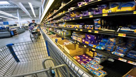 POV-while-pushing-a-cart-past-partially-empty-refrigerated-shelves-meant-for-cheese-products-and-other-customers