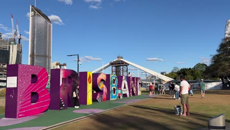 Tourists-visiting-the-iconic-landmark-at-river-bank,-colorful-giant-block-sign-of-Brisbane-City-with-cross-river-bridge-under-construction-in-the-background,-Queensland-the-sunshine-state,-Australia