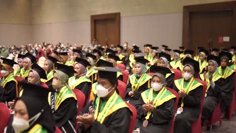 Graduados-Felices-Con-Sombreros-Y-Túnicas-Sentados-En-Fila-Y-Aplaudiendo