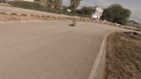 FPV-Aéreo-Persigue-A-Un-Niño-Pequeño-En-Una-Pequeña-Motocicleta-En-Una-Pista-De-Carreras-Amateur