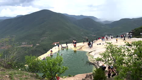 Vista-Panorámica-En-Plataforma-Rodante-Del-Sitio-Termal-Natural-En-La-Cima-De-La-Montaña,-Hierve-El-Agua,-San-Lorenzo-Albarradas,-Oaxaca-México,-Turistas-Que-Visitan-Refrescantes-En-La-Piscina-De-La-Cuenca-De-Aguas-Minerales-Al-Borde-De-La-Montaña