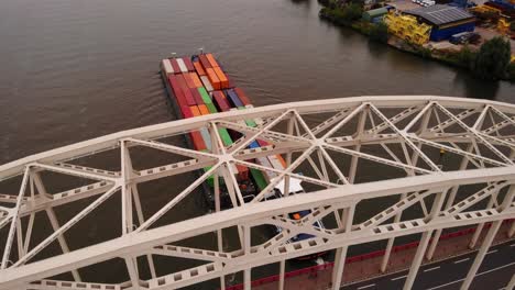 Vista-Aérea-A-Través-Del-Puente-Sobre-El-Norte-De-Maas-Barcaza-De-Remolque-Que-Transporta-Contenedores-De-Carga-A-Lo-Largo-Del-Río-Que-Pasa