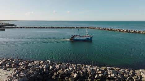 Eine-Luftaufnahme-Eines-Kleinen-Fischerbootes,-Das-An-Einem-Sonnigen-Frühlingsabend-Durch-Das-Hafentor-Aufs-Offene-Meer-Fährt