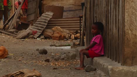 Un-Niño-Africano-Se-Sienta-En-El-Alféizar-De-Una-Casa-En-Ruinas-Mientras-Que-En-El-Fondo-Los-Animales-Caminan-Por-El-Suelo-Sucio---Cerrar