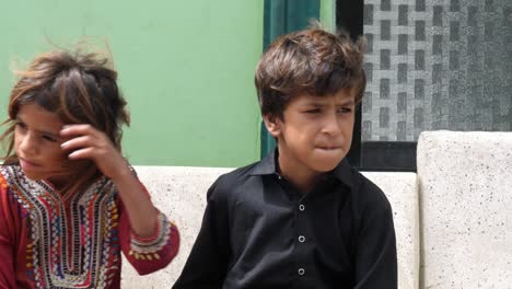Zwei-Kleine-Jungen-Und-Ein-Junges-Mädchen-Sitzen-Auf-Der-Bank-Am-Straßenrand-In-Sindh,-Pakistan
