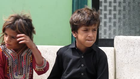 Two-young-boy-and-a-young-girl-sitting-in-the-bench-at-side-of-the-road-in-Sindh,-Pakistan