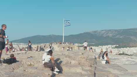 Turistas-Sentados-Alrededor-De-La-Bandera-Griega-Sobre-La-Acrópolis