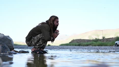 Langhaariger,-Bärtiger-Pakistanischer-Mann,-Der-Sein-Gesicht-Aus-Dem-Fluss-Wäscht