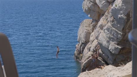 Un-Joven-Caucásico-Saltando-De-Acantilados-Rocosos-En-El-Casco-Antiguo-De-Dubrovnik,-Croacia.