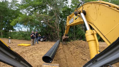 POV-while-operating-hydraulic-excavator-to-use-the-bucket-to-lightly-dig-and-tamp-dirt-in-bottom-of-drainage-ditch-at-pond-construction-site